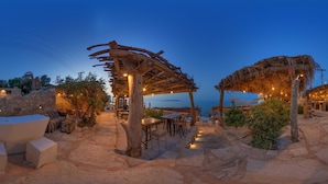 Un restaurante frente a la playa con terraza, paredes de piedra y luces colgantes.