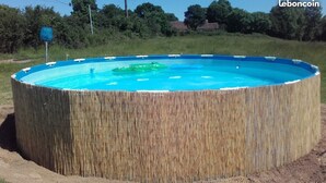 Una piscina circular con revestimiento similar a bambú, rodeada de césped y árboles.