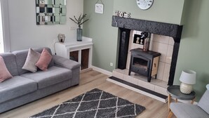 Una sala de estar con un sofá gris, un alfombra blanco y negro, una chimenea y un reloj de pared.