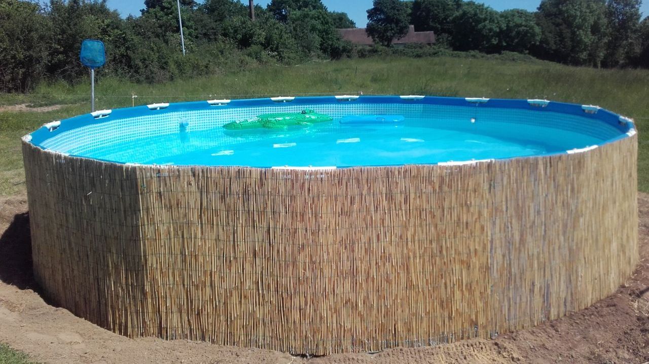 Una piscina circular con revestimiento similar a bambú, rodeada de césped y árboles.
