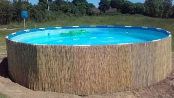 Una piscina circular con revestimiento similar a bambú, rodeada de césped y árboles.