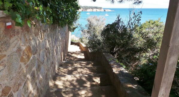 A stone staircase leading to a coastal area with boats in the background.