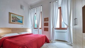 A bedroom with a bed, a window with curtains, a radiator, and a wall-mounted picture.