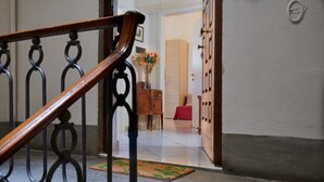 A staircase with a wooden handrail leading to a room with a wooden cabinet, a red chair, and a vase with flowers.