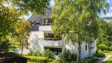 Ein modernes, zweistöckiges Haus mit Balkon, umgeben von üppigem Grün und einem gepflegten Rasen.