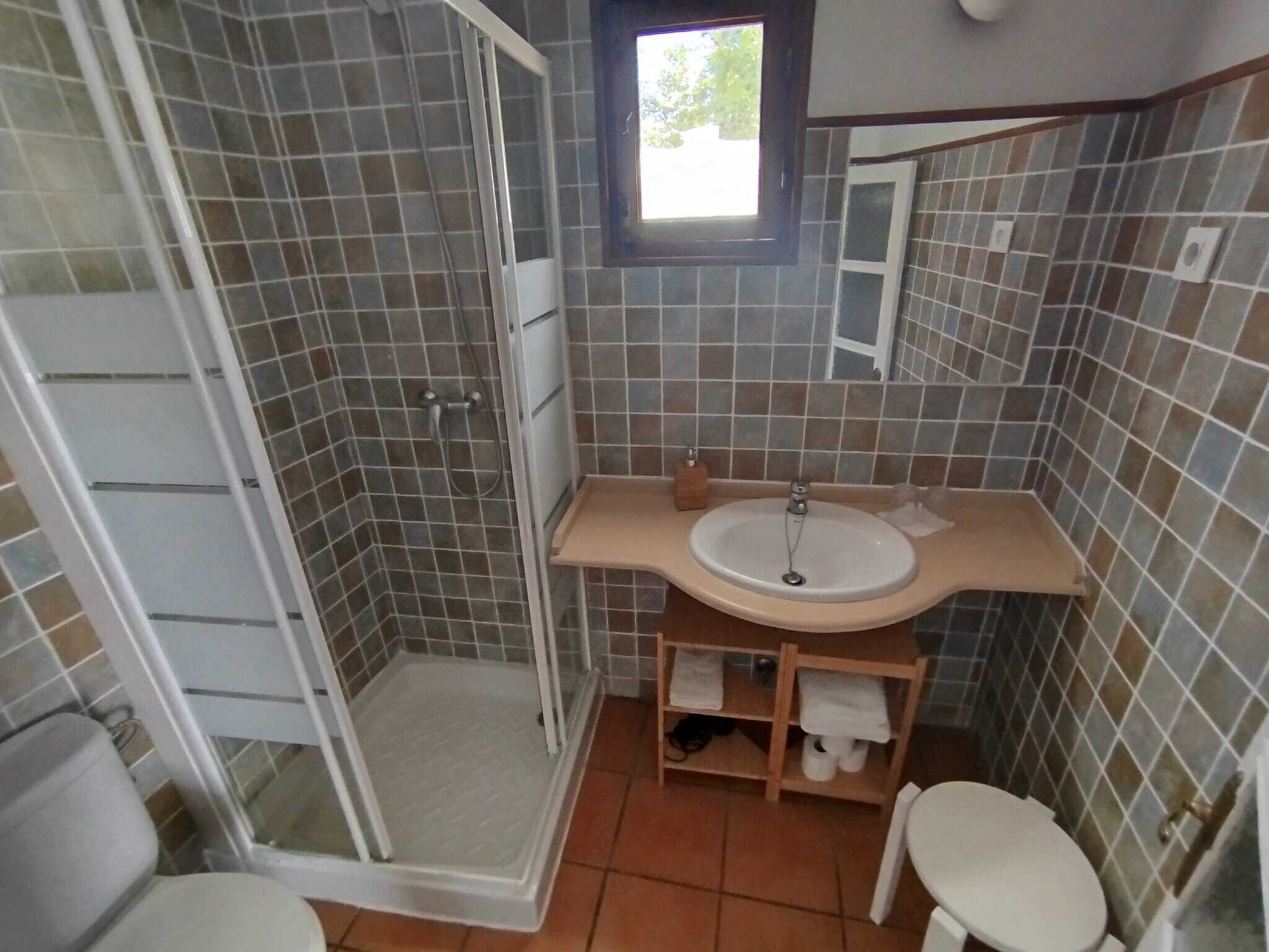 A bathroom with a shower, sink, toilet, and a small window.