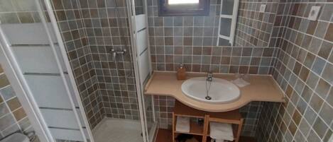 A bathroom with a shower, sink, toilet, and a small window.