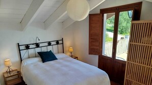 Een slaapkamer met een bed, twee bedlampen, een houten deur en uitzicht op groen.