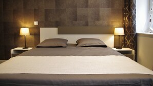 Een net opgemaakt bed met een hoofdbord, twee bedlampjes en een raam met gordijnen.