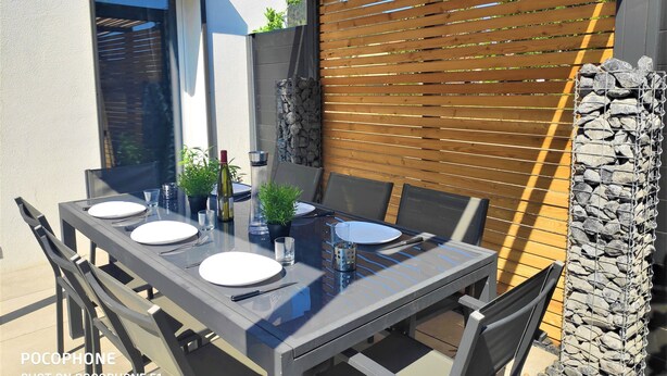 Een terras buiten met een tafel gedekt voor vier personen, inclusief borden, bestek en een fles.