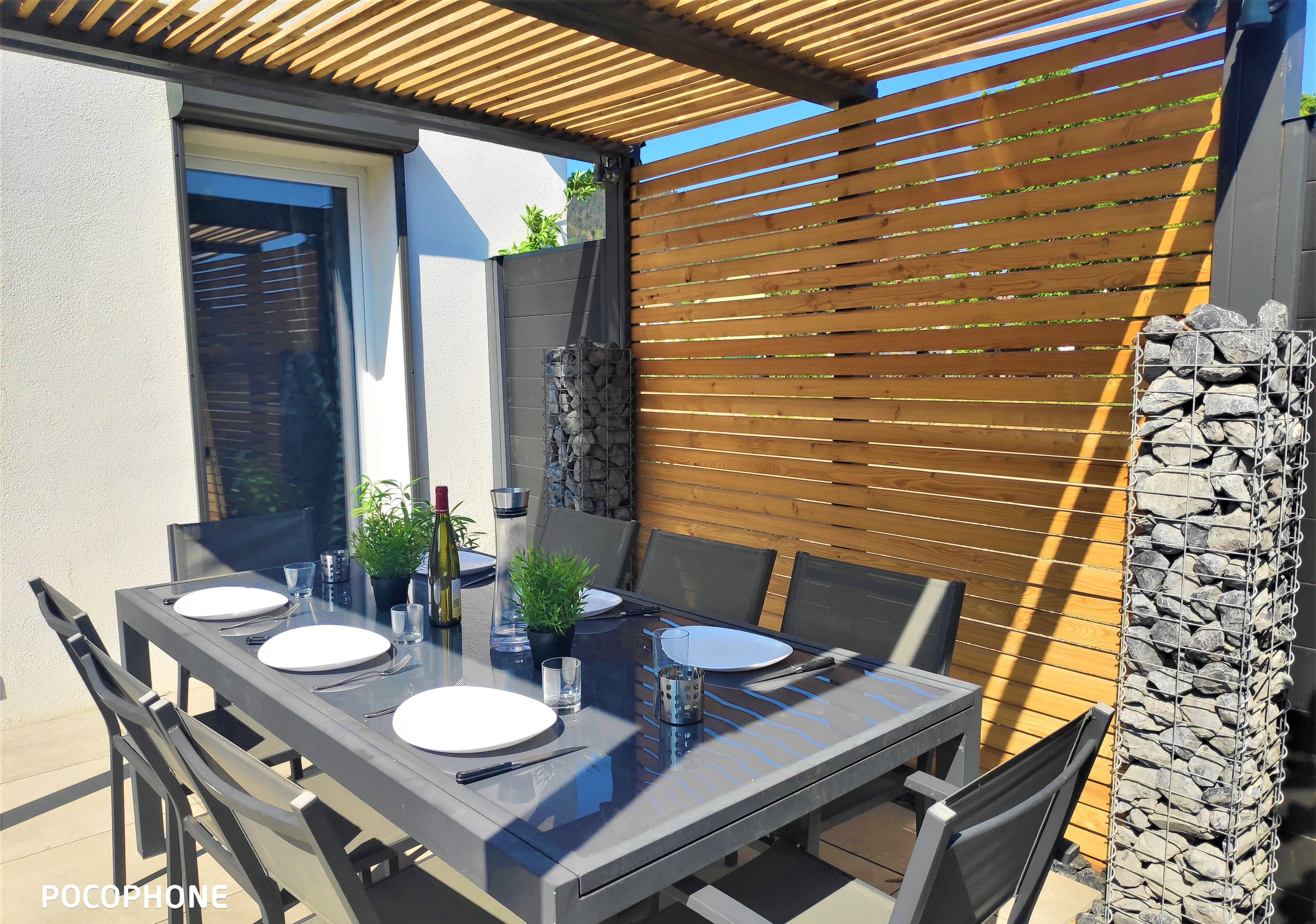 An outdoor patio with a table set for four, including plates, cutlery, and a bottle.