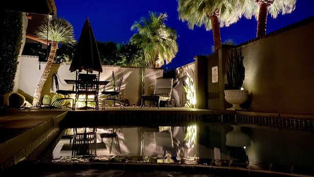 An outdoor pool area with a table and chairs, palm trees, and a wall with a sign. - Beautiful & Romantic Downtown Private Pool & Spa.  Amazing Westerly facing views (Palm Springs)