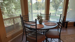 Comedor con una mesa redonda, seis sillas, individuales tejidas y una planta en maceta.