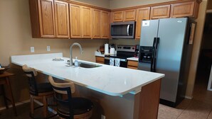 Una cocina con armarios de madera, un refrigerador de acero inoxidable, un microondas y un fregadero.