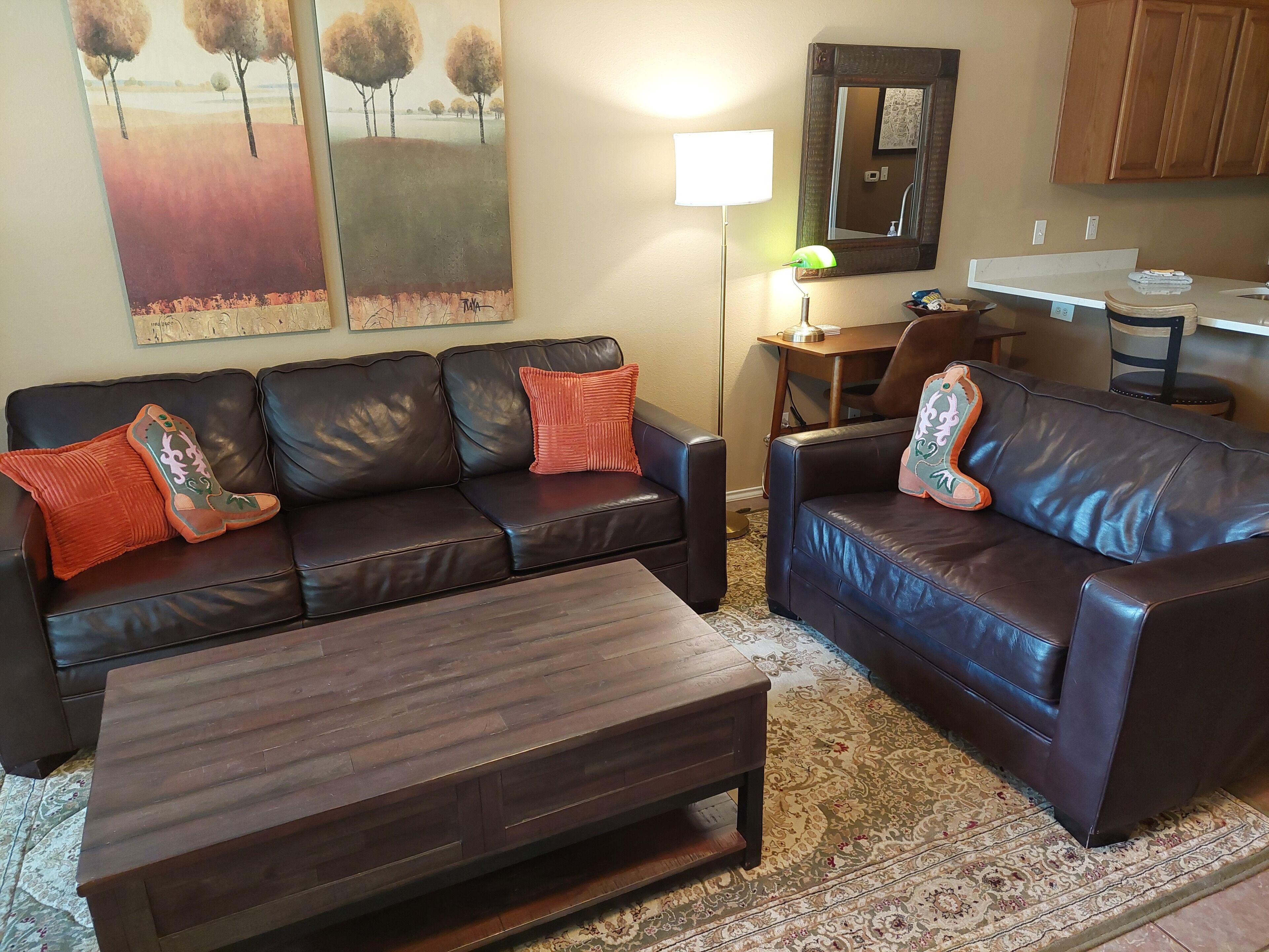 A living room with two leather sofas, a wooden coffee table, a lamp, a mirror, and a painting on the wall.