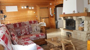 Acogedor interior de cabaña de madera con un sofá de madera, una chimenea y una mesa de comedor.
