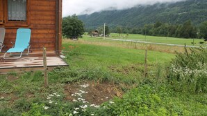 Una cabaña de madera con un porche, una silla azul y vistas a un valle verde y montañas.