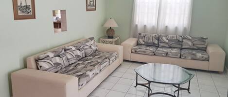 A living room with two sofas, a glass coffee table, and framed pictures on the wall.