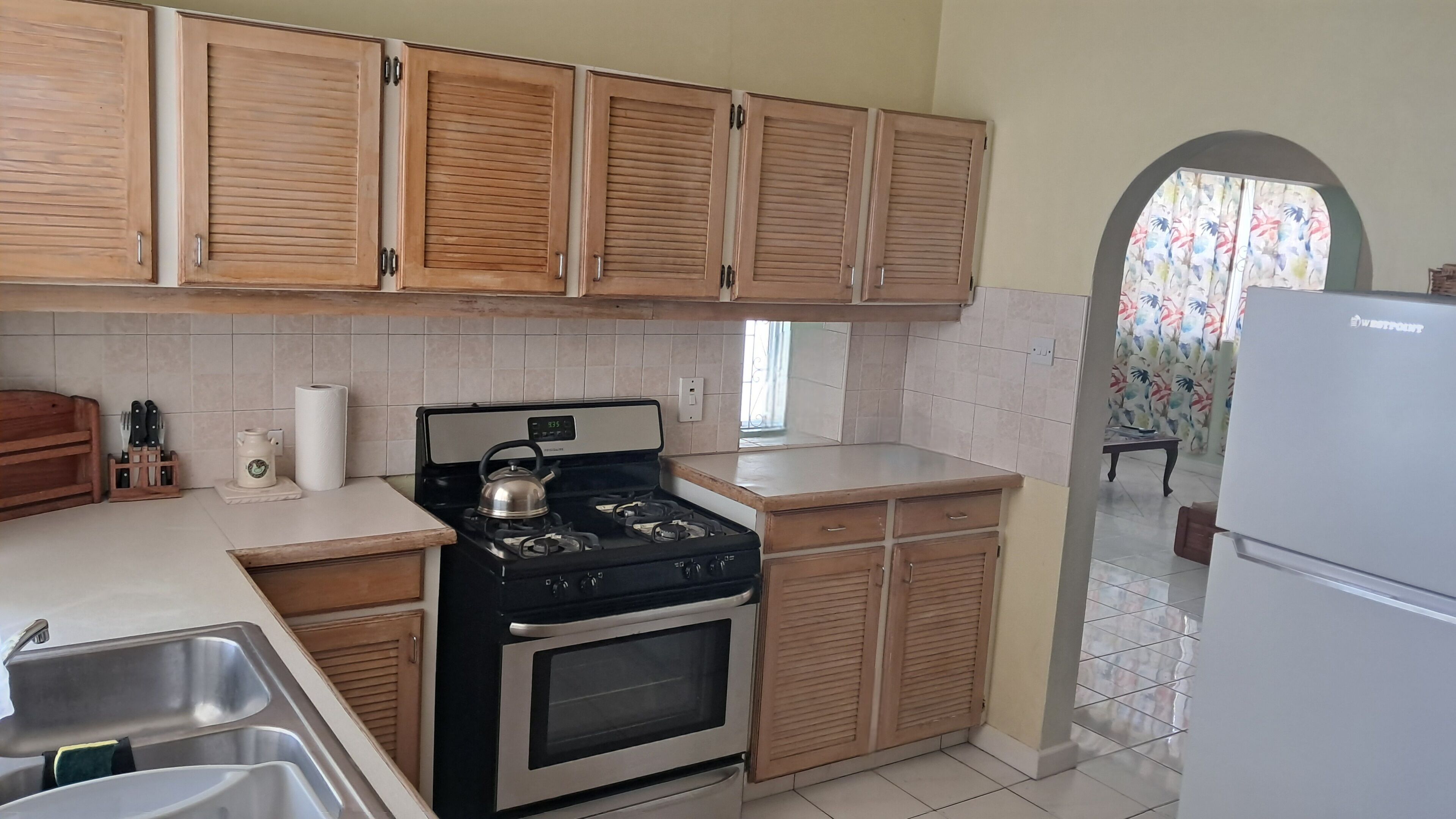 Une cuisine avec des meubles de rangement en bois, une cuisinière à gaz, un four, un évier et un réfrigérateur.