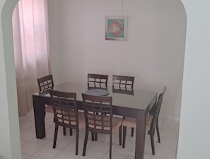 Un comedor con una mesa redonda y seis sillas, un cuadro enmarcado en la pared y una ventana con cortinas.