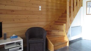 A staircase with wooden steps and a handrail, a grey armchair, and a white entertainment unit with a remote control.