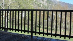 A wooden deck with a metal railing overlooking a mountainous landscape with trees and a snow-capped peak.
