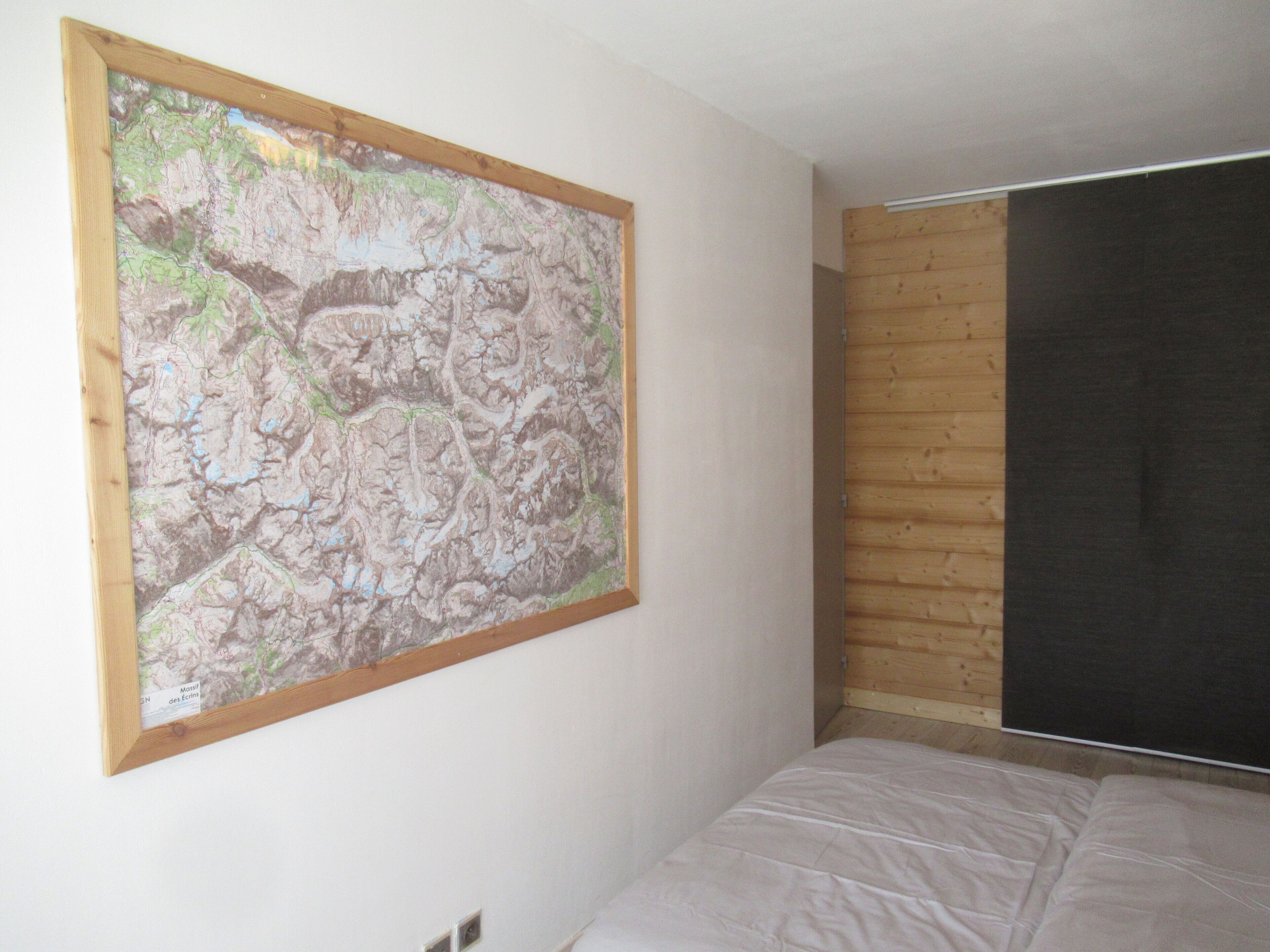 Een slaapkamer met een bed, een houten hoofdeinde, een grote kaart aan de muur en een raam met houten jaloezieën.