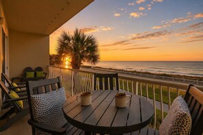 A balcony with a wooden table and chairs, overlooking a beach at sunset. - Pet Friendly, Gulf Front Beach Retreat 209 Beach Service (Miramar Beach)