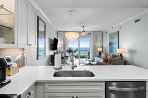 A modern kitchen with a central island, a dining area with a view, and a living room with a sofa and a TV.