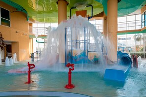 A water play area with multiple water jets and slides, surrounded by large windows and columns.
