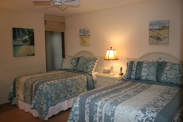 A bedroom with two beds, a nightstand with a lamp, and wall art.