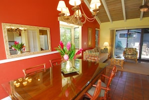 A dining area with a glass table, chairs, a vase of flowers, and a chandelier. - Gorgeous Greenbelt!  Home with beautiful mountain views & 5 min walk from beach! (Koloa)