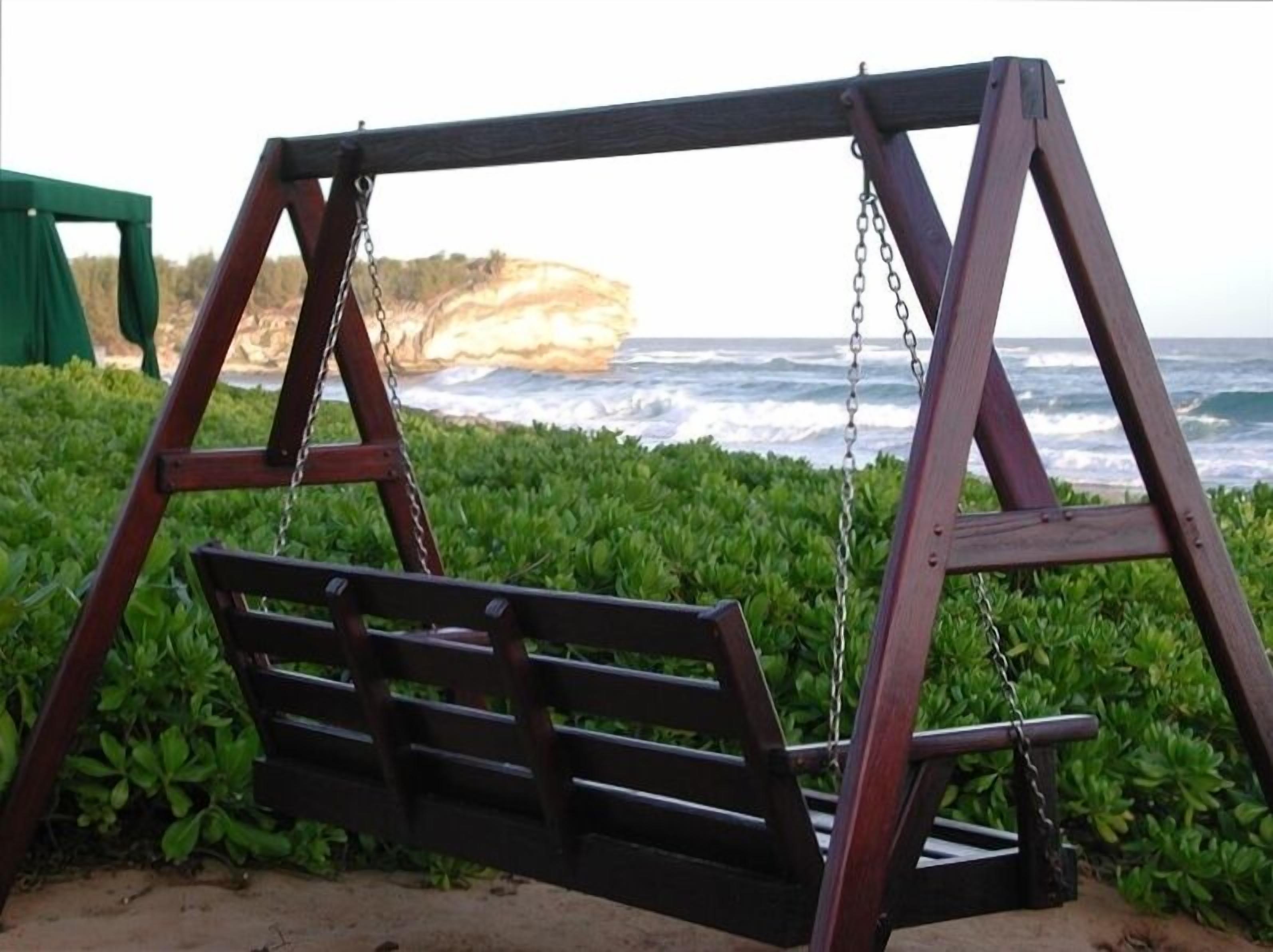 Un columpio de madera con un banco, cerca de una costa rocosa con follaje verde.