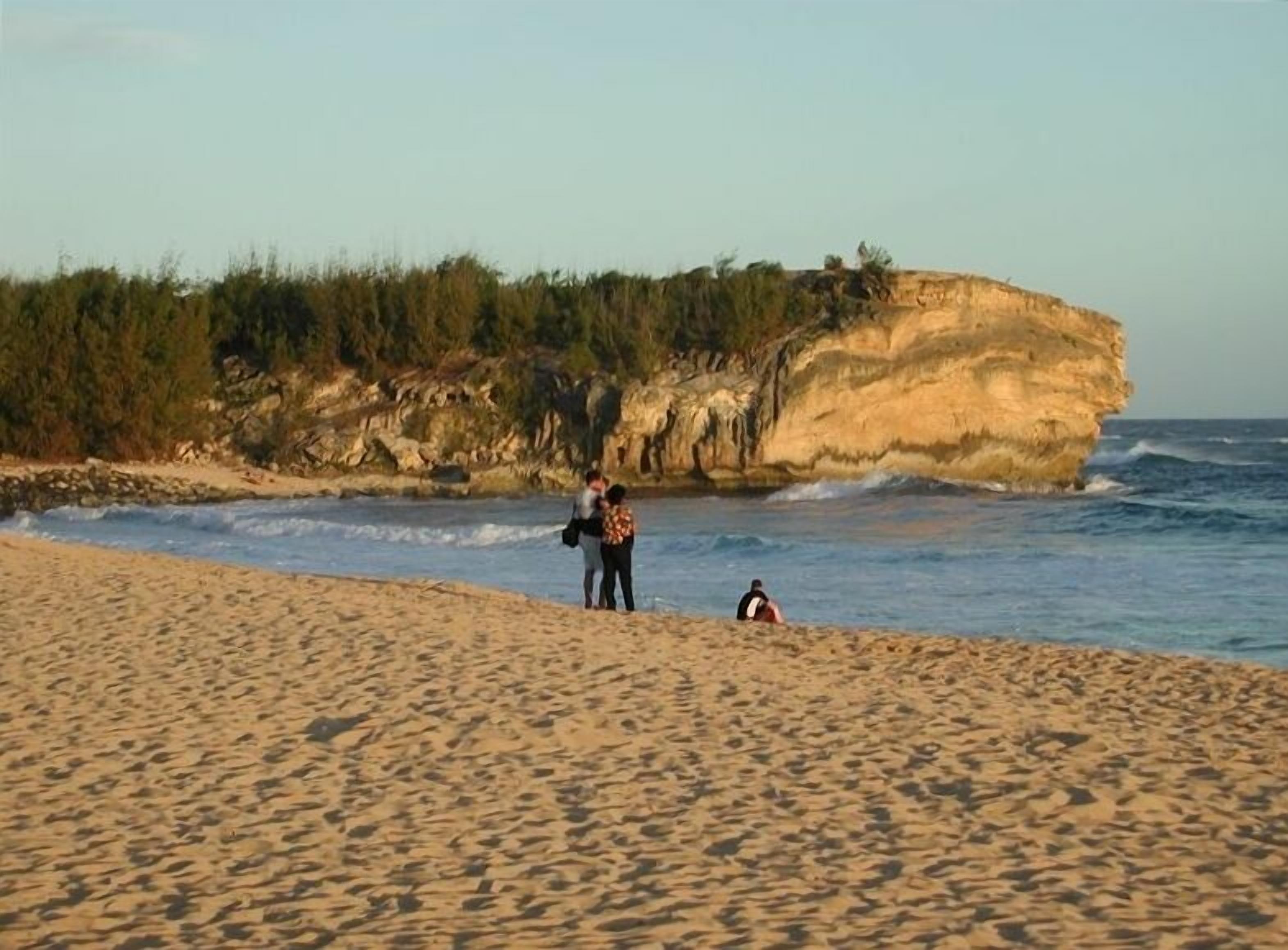 Una playa con un acantilado rocoso al fondo.