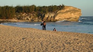Uma praia com um penhasco rochoso ao fundo.