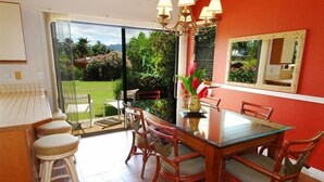 Uma sala de jantar com mesa de vidro, cadeiras de vime, parede vermelha e um espelho grande.