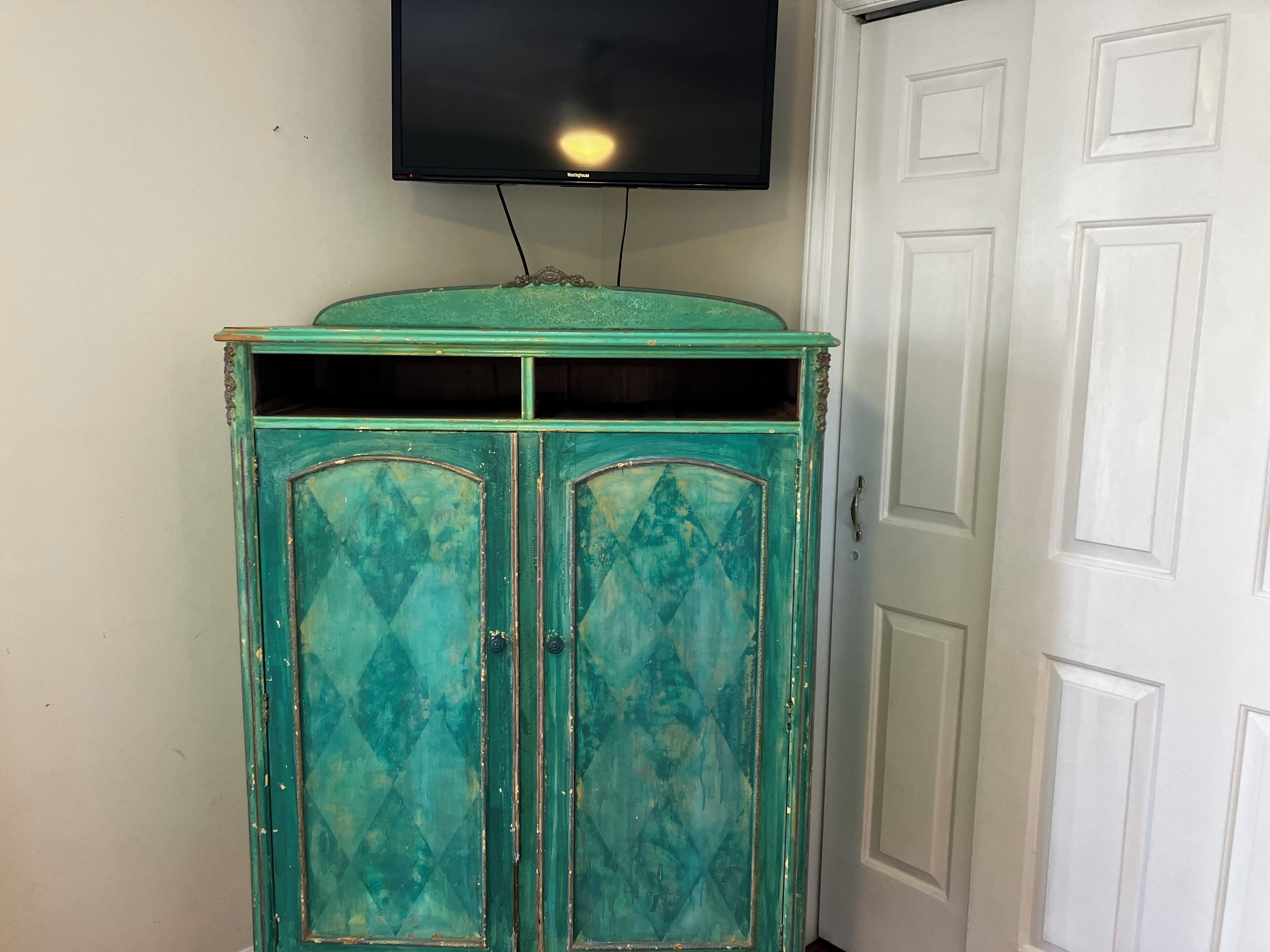 A teal cabinet with two doors, a television mounted above it, and a white door to the right.