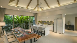 Una cocina moderna con armarios blancos, una isla central y un comedor con mesa y sillas de madera.