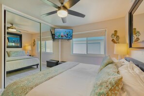 Una habitación de hotel con cama, ventilador de techo, televisión y ventana.