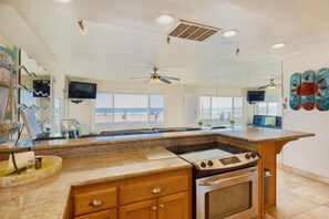 A kitchen with a central island, built-in oven, and a large window overlooking the beach.