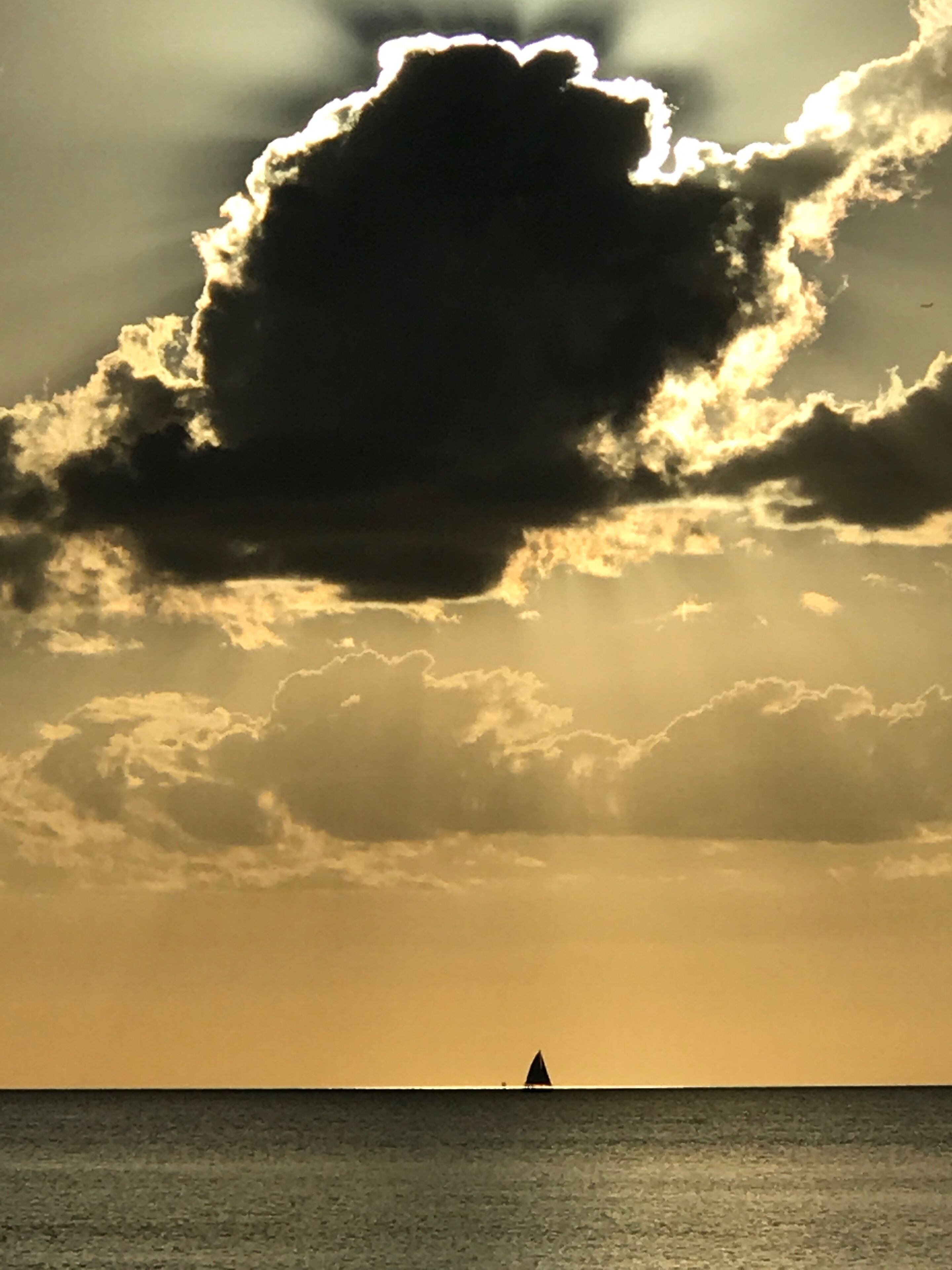 A sailboat on calm waters under a dramatic sky with a large cloud formation.