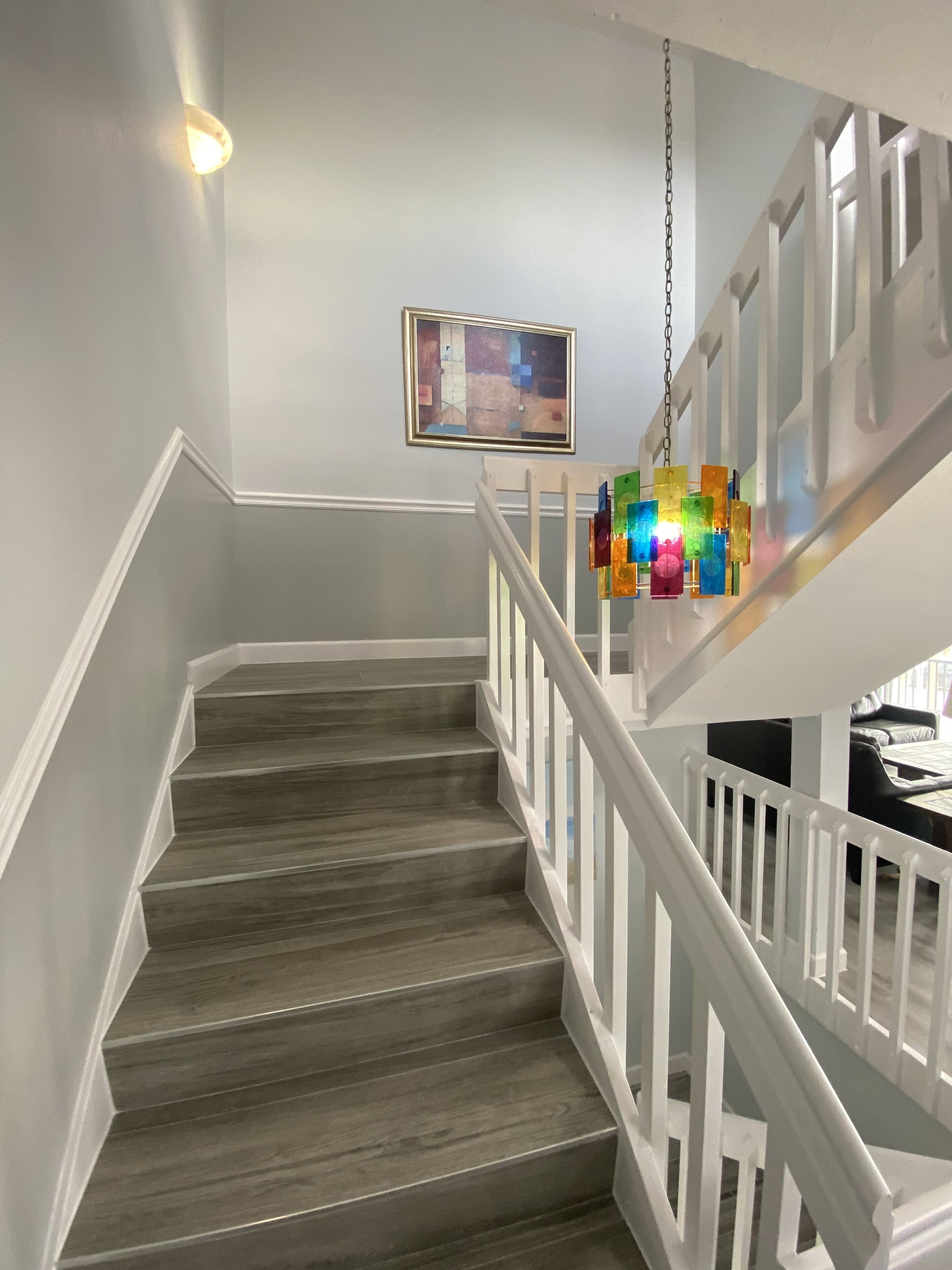 A staircase with wooden steps and white railings, a hanging colorful light fixture, and a framed picture on the wall.