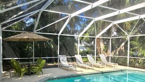 Una piscina exterior con cerramiento de vidrio, rodeada de sillones de descanso y una mesa con sombrilla.