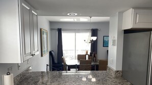 Una cocina con encimera de granito, armarios blancos y una zona de comedor con sillas de mimbre.