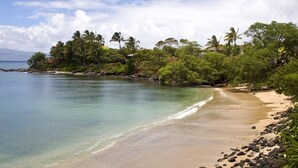 Une plage à l’eau turquoise et limpide, bordée d’un rivage sablonneux et d’une végétation luxuriante.