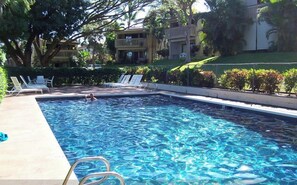 Une piscine rectangulaire à l’eau d’un bleu cristallin, entourée de chaises longues et d’une clôture.
