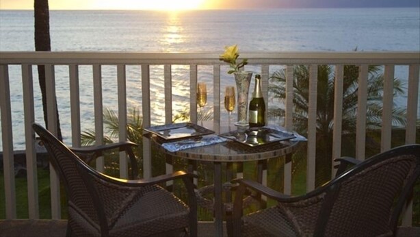 Un balcon avec des fauteuils en osier et une table dressée pour deux personnes, d’où l’on peut admirer le coucher de soleil sur l’océan.