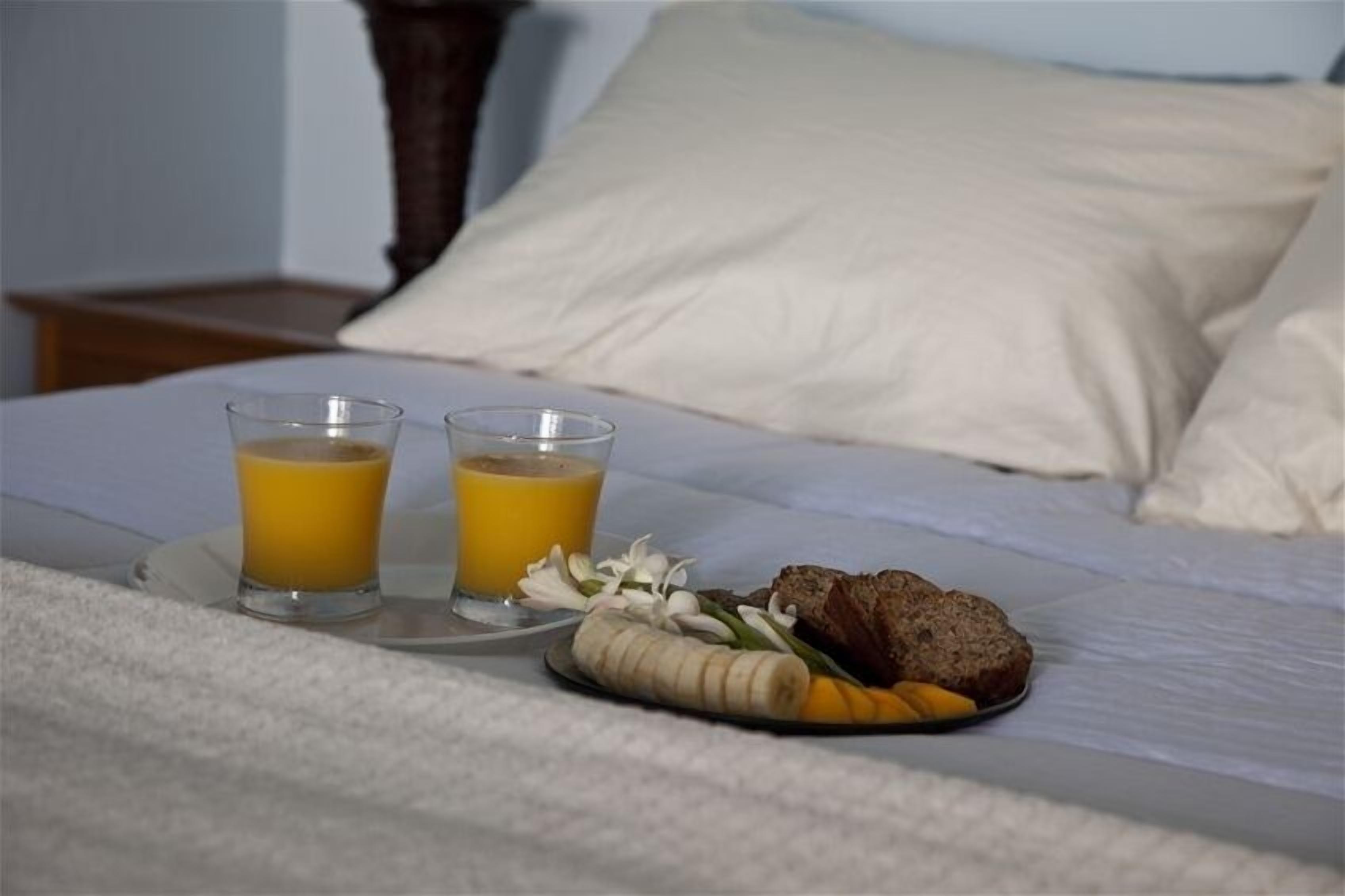 Un lit bien fait, sur lequel se trouve un plateau avec une assiette de nourriture, deux verres de jus d’orange et une banane.