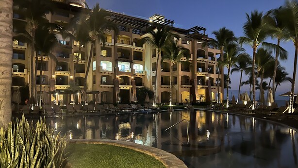 Un hotel amb una piscina ampla, palmeres i una façana d'edifici ben il·luminada.