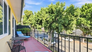 A balcony with a red tiled floor, two metal chairs with blue cushions, and a small round table.